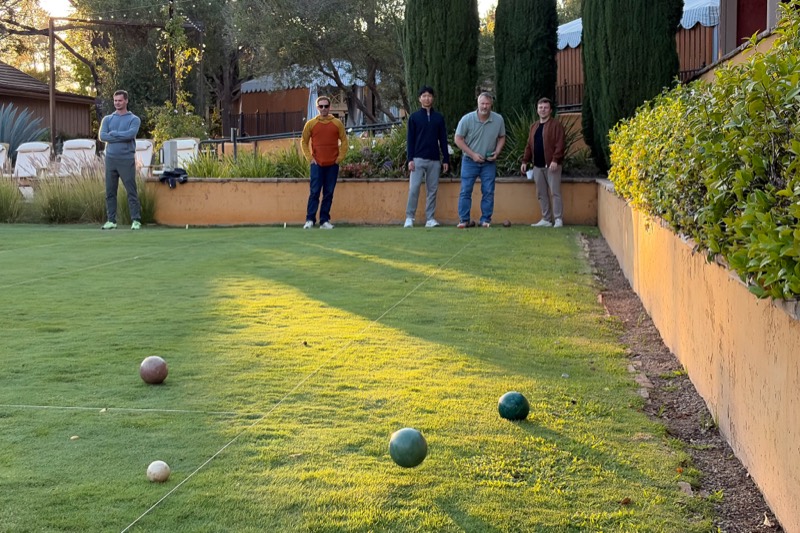 Team members playing bocce on a lawn at sunset